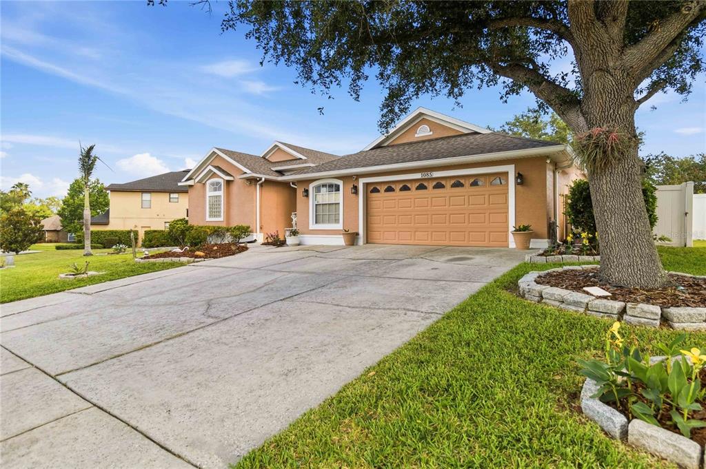 A single-story tan house with a two-car garage and a large tree in the front yard — 1085 CHASE DRIVE, WINTER GARDEN, FL