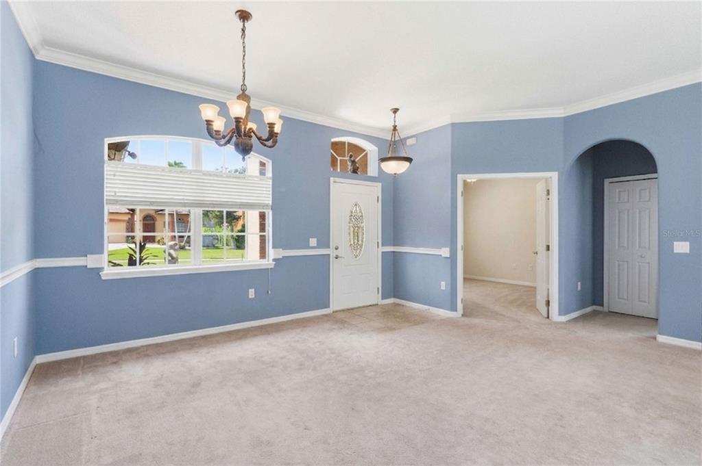 A blue-walled room features beige carpeting, a white front door, and two hanging light fixtures — 1085 CHASE DRIVE, WINTER GARDEN, FL
