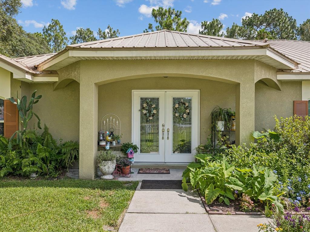 A light green house exterior features a covered entryway with double glass doors and landscaping — 12229 BARNEVELDE ROAD, WEEKI WACHEE, FL