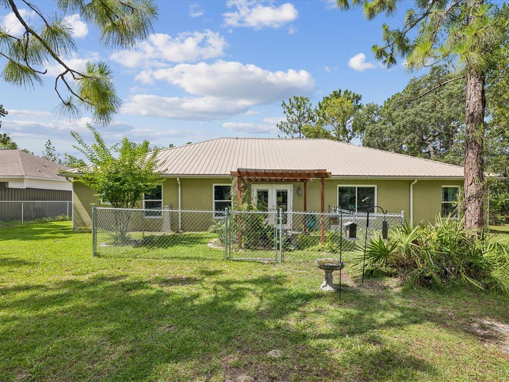 The back of a single-story house features a metal roof, stucco walls, and a fenced yard — 12229 BARNEVELDE ROAD, WEEKI WACHEE, FL