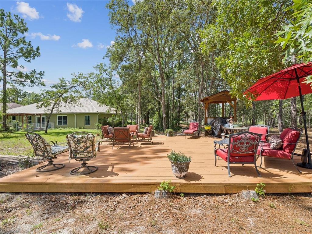 A wooden deck with outdoor furniture and a red umbrella sits in a wooded yard — 12229 BARNEVELDE ROAD, WEEKI WACHEE, FL