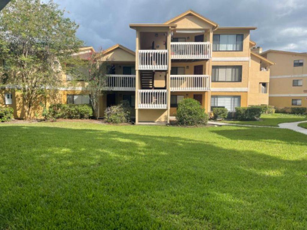 A three-story apartment building with tan stucco siding and white balcony railings faces a lawn — 1550 S BELCHER ROAD UNIT 324, CLEARWATER, FL