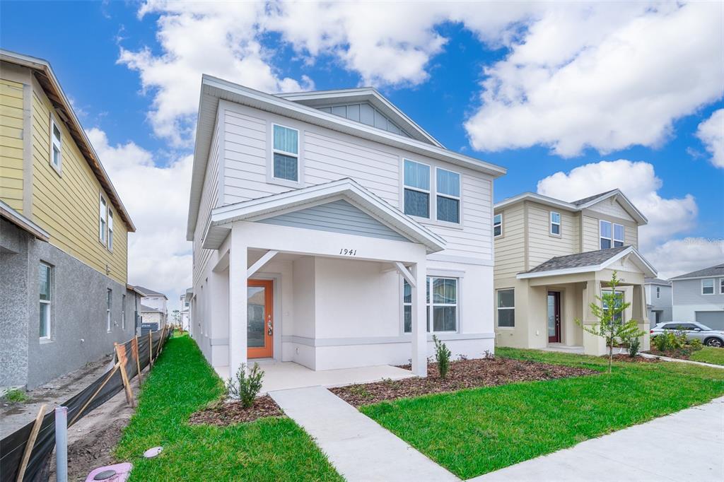 A two-story house with white siding, a covered front porch, and an orange front door — 1941 SUMMER SERENITY DRIVE, KISSIMMEE, FL