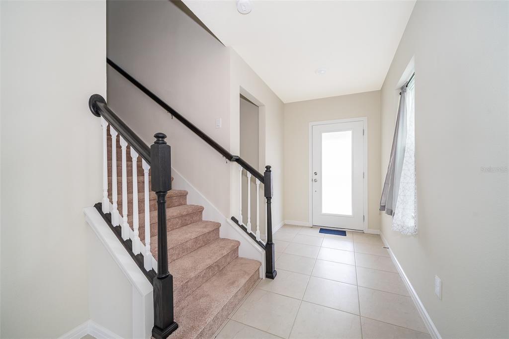 An entryway features a carpeted staircase with dark wood railings and light tile flooring — 1941 SUMMER SERENITY DRIVE, KISSIMMEE, FL