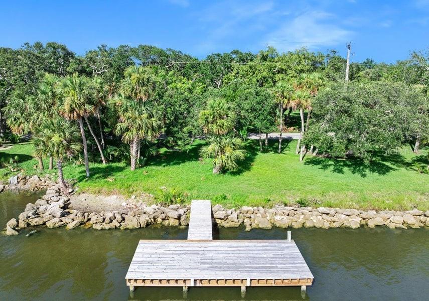 A wooden dock extends from a rocky shoreline into the water in front of trees — 2841 JOHN ANDERSON DRIVE, ORMOND BEACH, FL