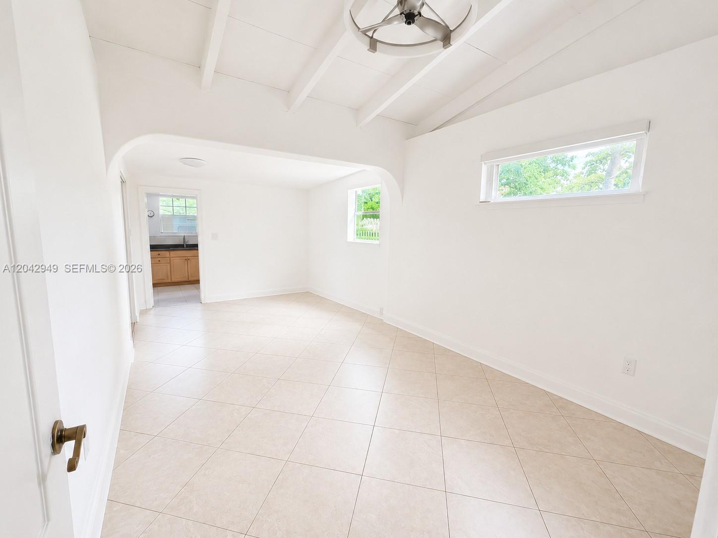 A bright, empty room features white walls, tile flooring, and a vaulted ceiling with exposed beams — 401 NW 198th St, Miami Gardens FL 33169, MIAMI GARDENS, FL