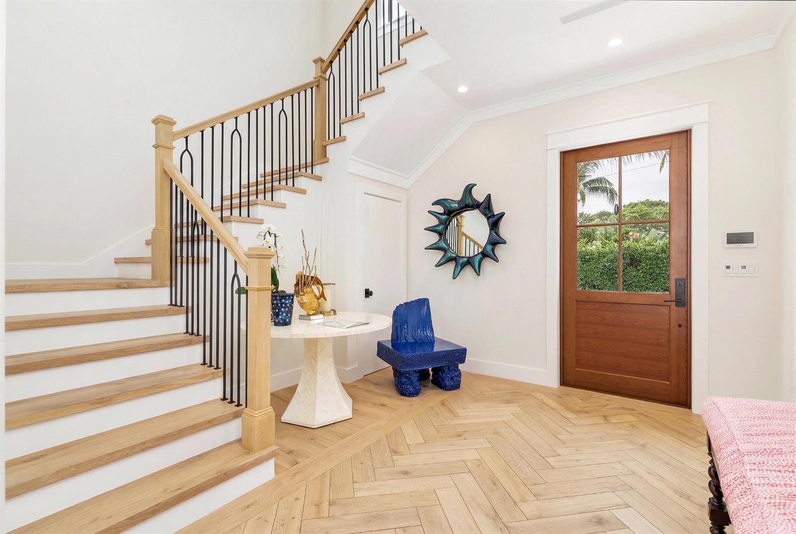 A bright entryway features a wooden staircase, herringbone flooring, a round table, and blue furniture — 315 Avila Road, West Palm Beach FL 33405, WEST PALM BEACH, FL