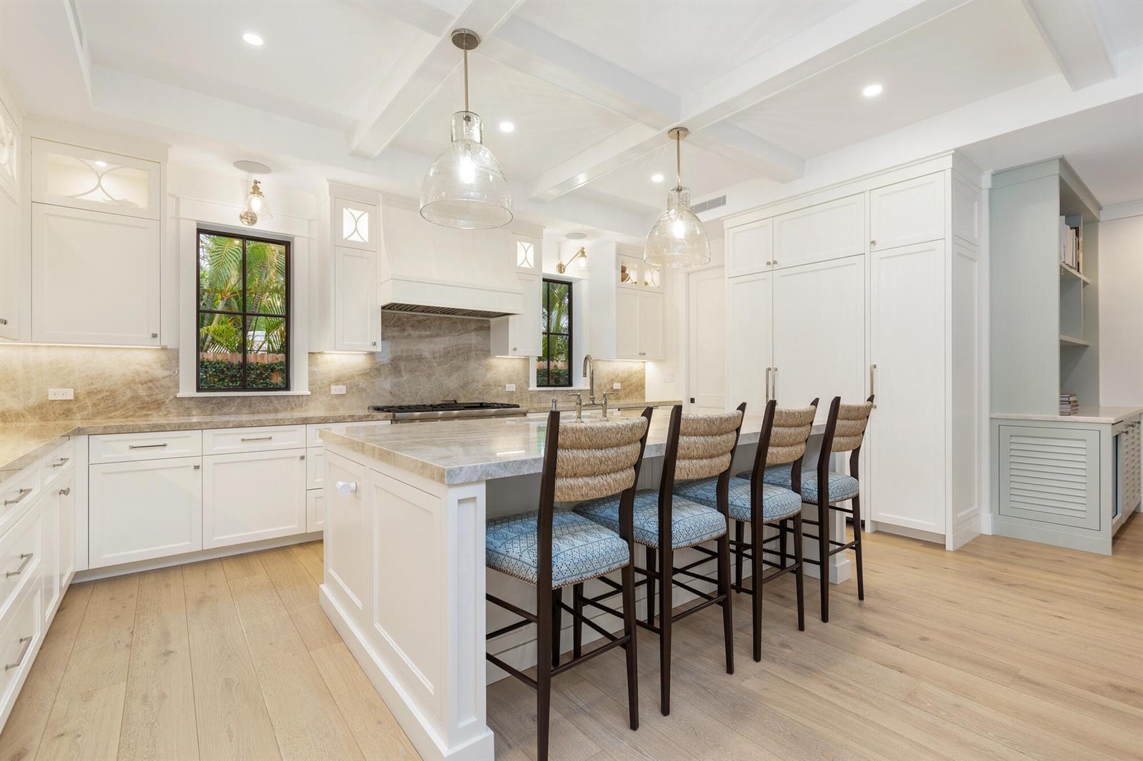 A bright kitchen features white cabinetry, a large marble-topped island, and four woven bar stools — 315 Avila Road, West Palm Beach FL 33405, WEST PALM BEACH, FL