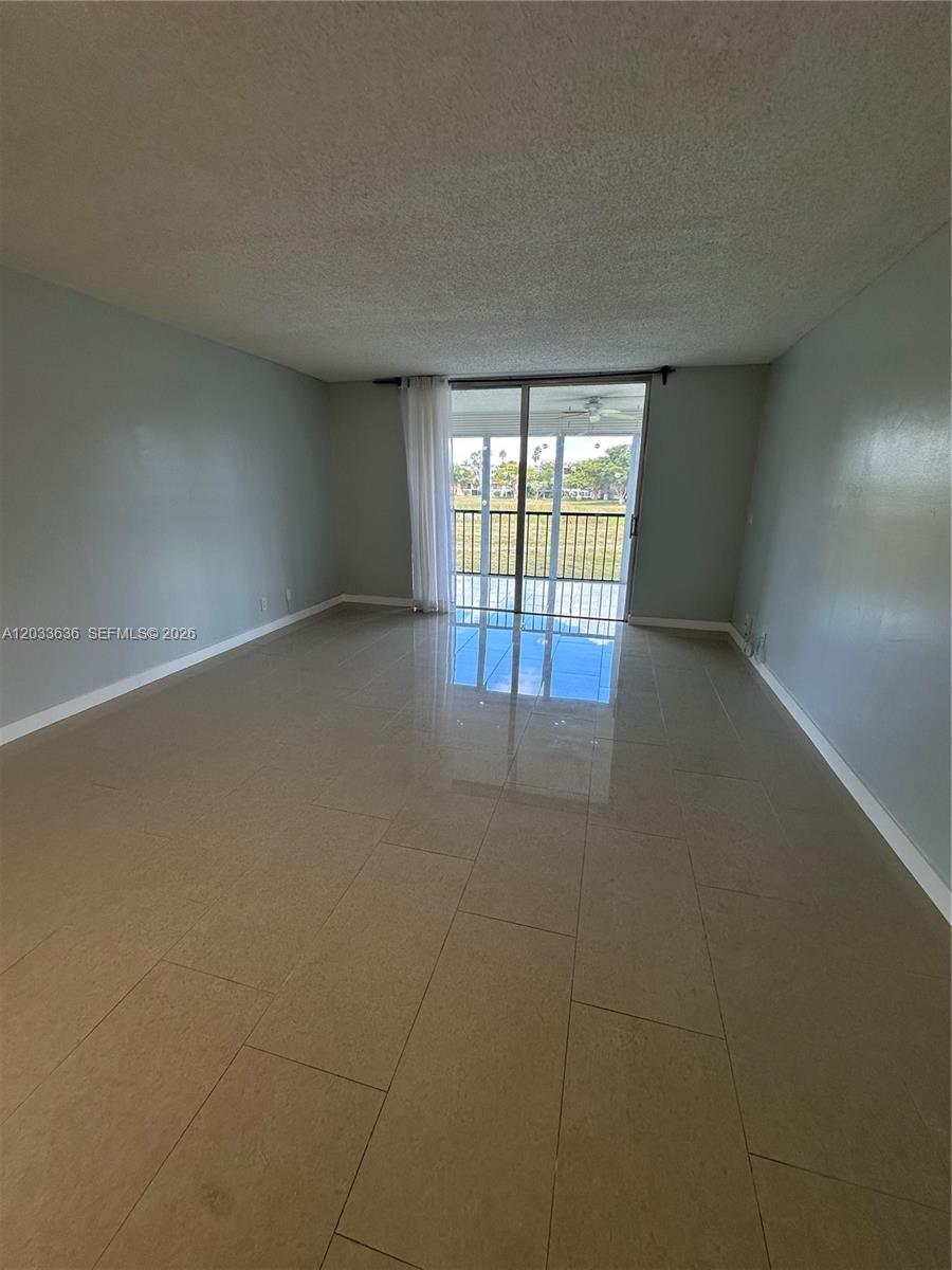 An empty living room features light-colored tile flooring, gray walls, and a sliding glass door — 7561 NW 1st St # 204, Margate FL 33063, MARGATE, FL