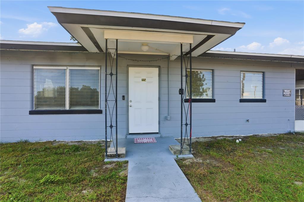 A light blue house exterior features a white front door under a flat roof overhang — 225 E POMELO STREET, LAKE ALFRED, FL