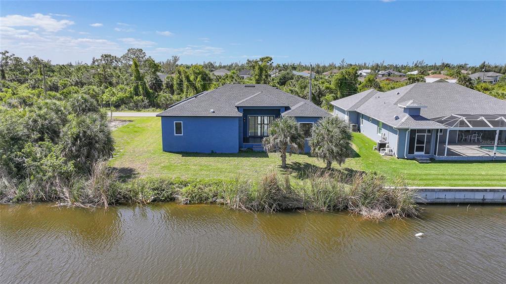 A blue house with a dark roof sits next to a canal and a neighbor — 15096 LAKELAND CIRCLE, PORT CHARLOTTE, FL