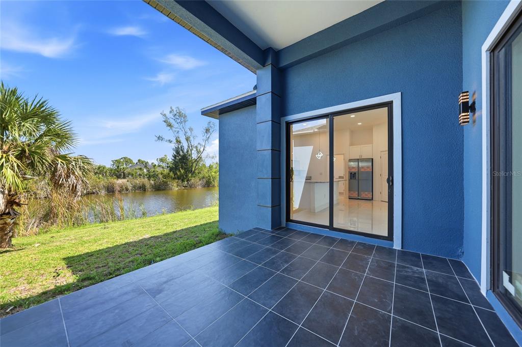 A covered patio with dark tile flooring overlooks a grassy yard and a small pond — 15096 LAKELAND CIRCLE, PORT CHARLOTTE, FL