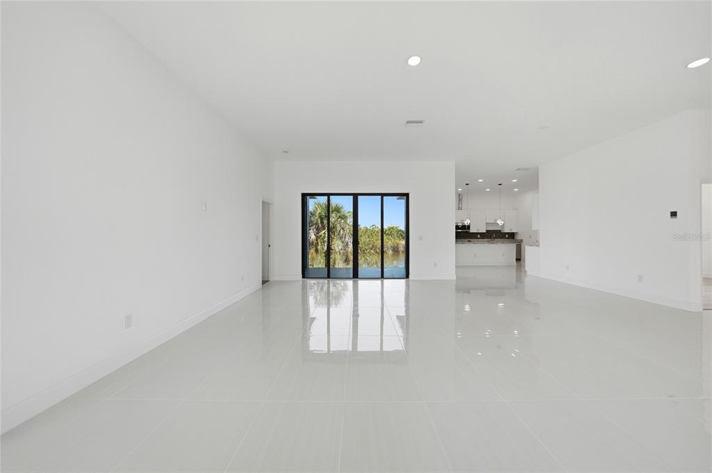 An open-concept living area features white tile flooring, recessed lighting, and sliding glass doors — 15096 LAKELAND CIRCLE, PORT CHARLOTTE, FL