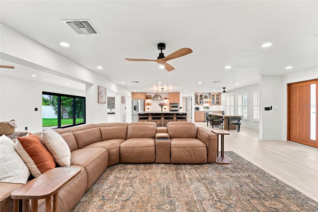 A spacious open-concept living room features a large leather sectional, wood flooring, and a kitchen — 6241 TANGLEWOOD DRIVE NE, ST PETERSBURG, FL