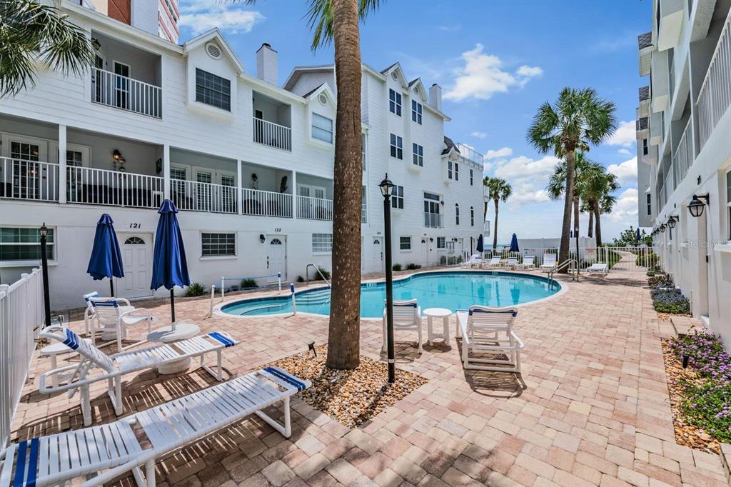 A swimming pool is surrounded by a brick patio, lounge chairs, and white buildings — 17960 GULF BOULEVARD UNIT 121, REDINGTON SHORES, FL