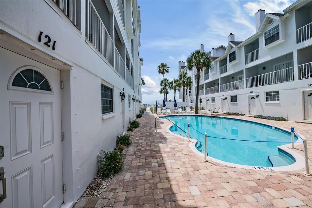 A swimming pool sits between two white multi-story apartment buildings with a brick walkway — 17960 GULF BOULEVARD UNIT 121, REDINGTON SHORES, FL