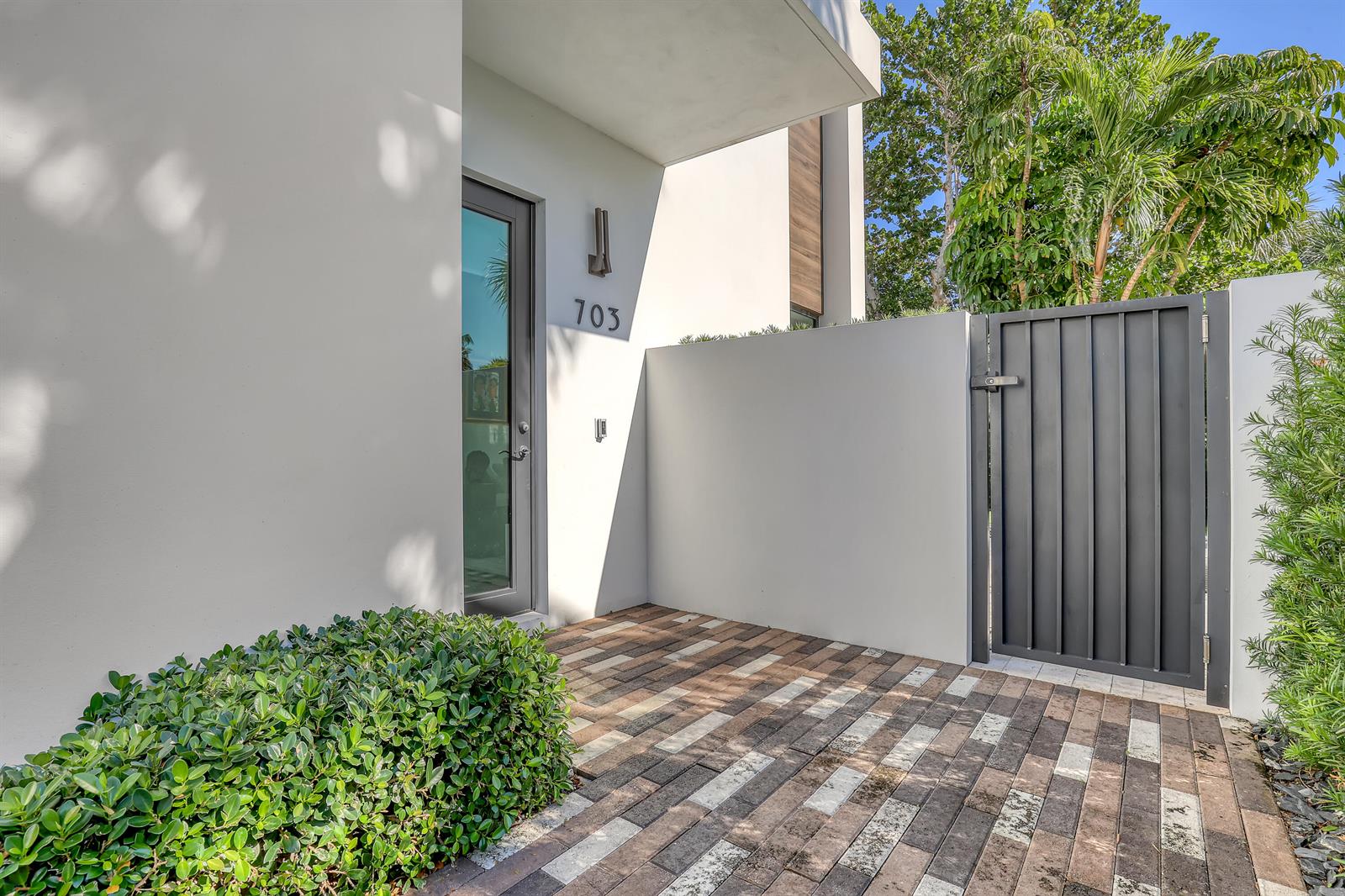 A modern home entrance features a glass door, a gray metal gate, and paver flooring — 703 NE 5th Street, Delray Beach FL 33483, DELRAY BEACH, FL