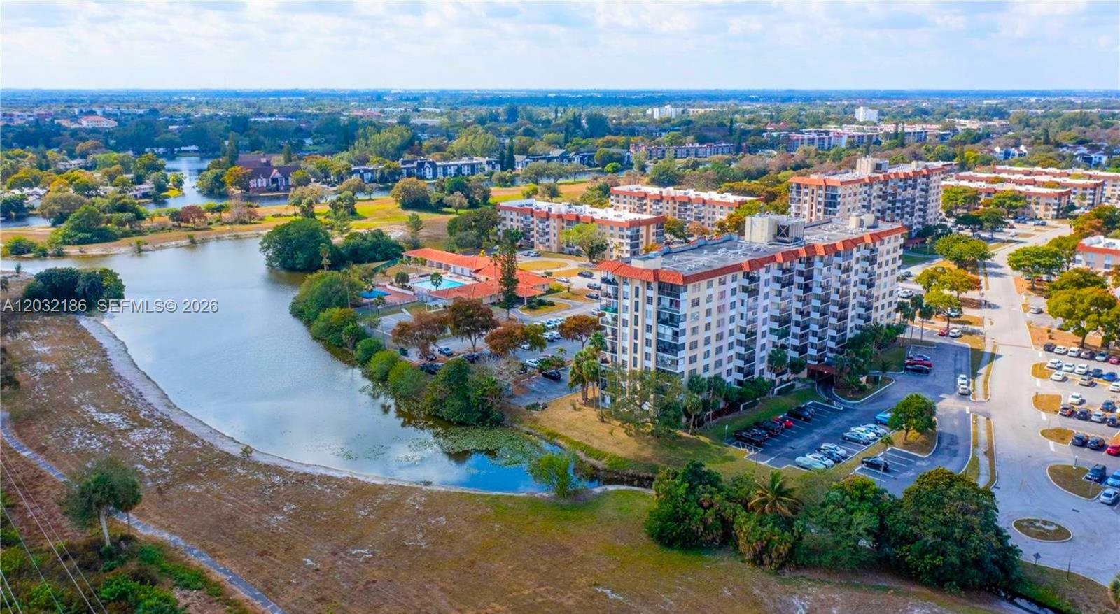 An aerial view shows a multi-story apartment building situated next to a lake and parking — 4164 Inverrary Dr # 204, Lauderhill FL 33319, LAUDERHILL, FL