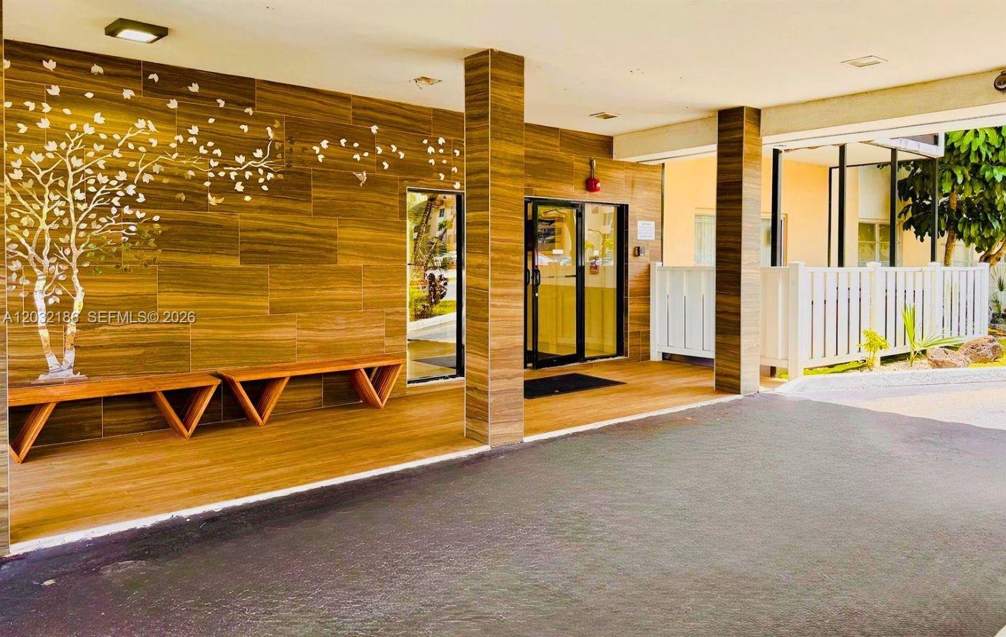 A covered building entrance features wood-look tile walls, a matching bench, and glass doors — 4164 Inverrary Dr # 204, Lauderhill FL 33319, LAUDERHILL, FL