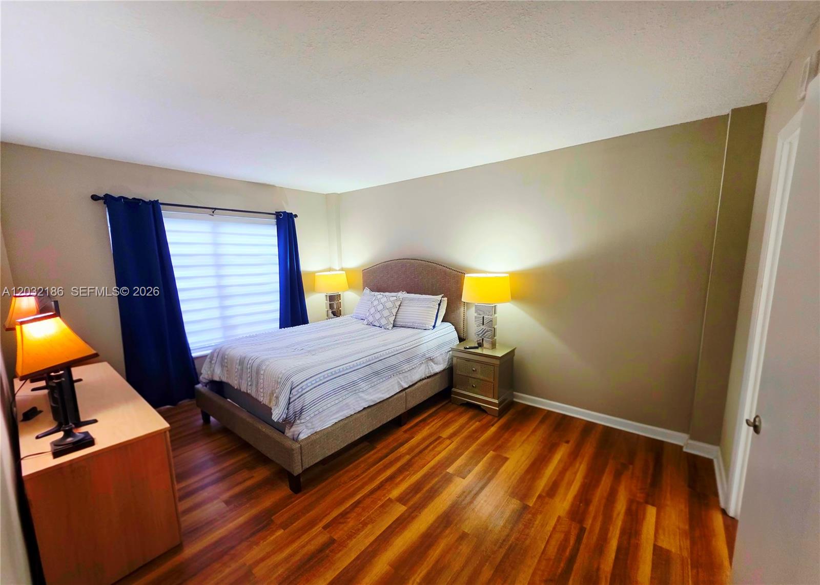 A bedroom features a bed with a gray headboard, wood flooring, and blue curtains — 4164 Inverrary Dr # 204, Lauderhill FL 33319, LAUDERHILL, FL
