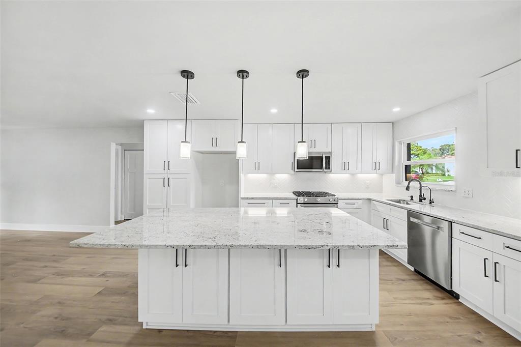A modern kitchen features white cabinets, a large granite island, and stainless steel appliances — 10604 WHITMAN CIRCLE, ORLANDO, FL