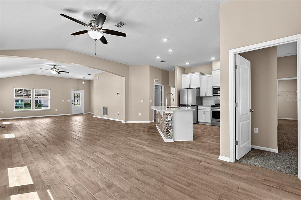An open-concept living area with wood-look tile floors, a kitchen island, and white cabinetry — 65 LOB WEDGE LANE, BUNNELL, FL