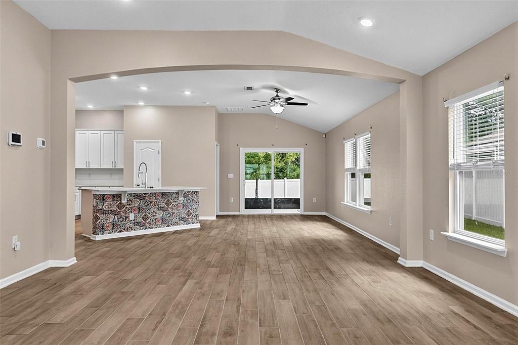 An open-concept living area features wood-look tile flooring, a patterned kitchen island, and vaulted ceilings — 65 LOB WEDGE LANE, BUNNELL, FL