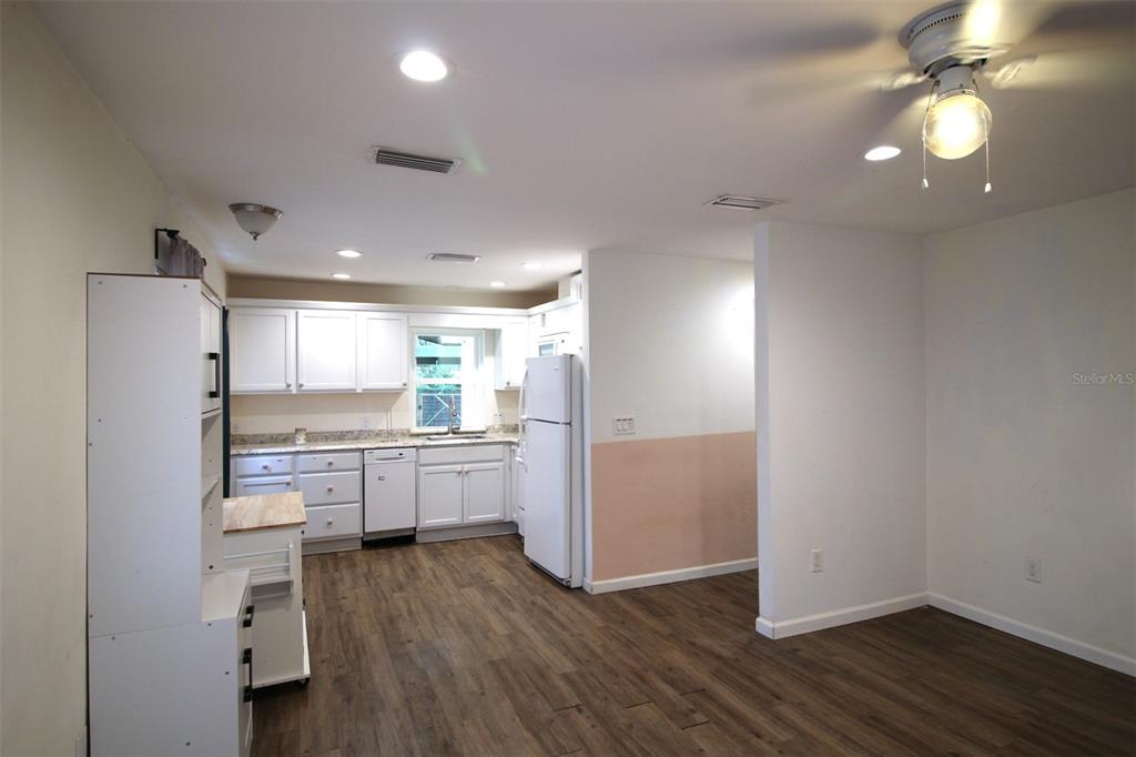 A kitchen with white cabinets, a white refrigerator, and wood-look flooring opens to a dining area — 17091 SW 138TH LANE, ARCHER, FL