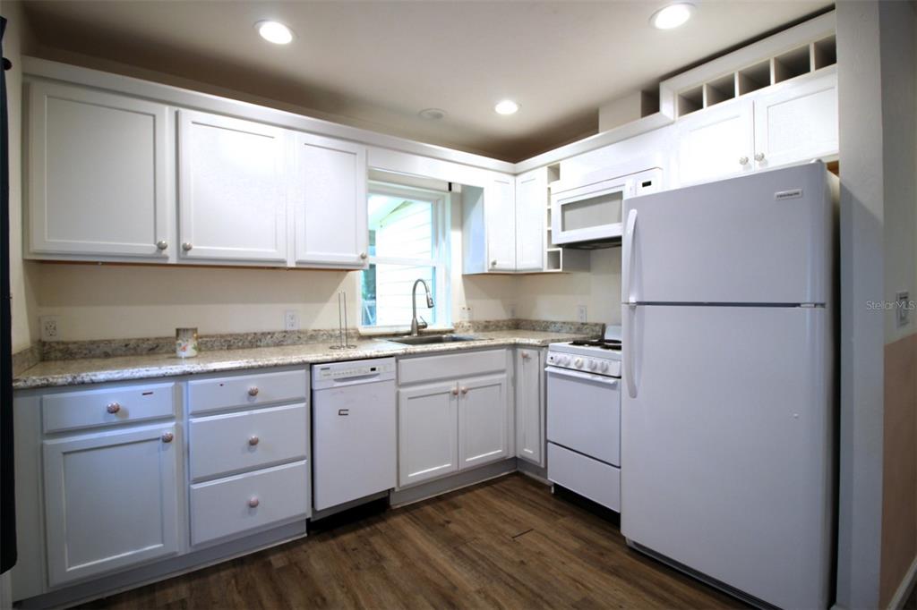 A kitchen with white cabinets, granite countertops, white appliances, and wood-look flooring — 17091 SW 138TH LANE, ARCHER, FL