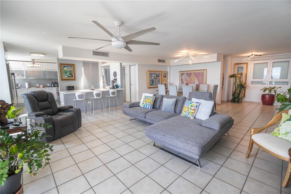 An open-concept living and dining area features tile flooring, a gray sectional, and a kitchen — 100 REINA DE CASTILLA UNIT 308, SAN JUAN, PR