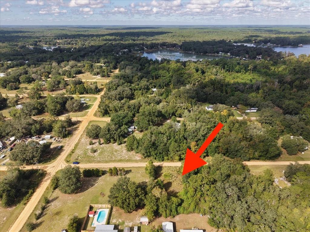 An aerial view shows a wooded, undeveloped lot bordered by a dirt road and trees — 206 N HELMERS AVENUE, INTERLACHEN, FL