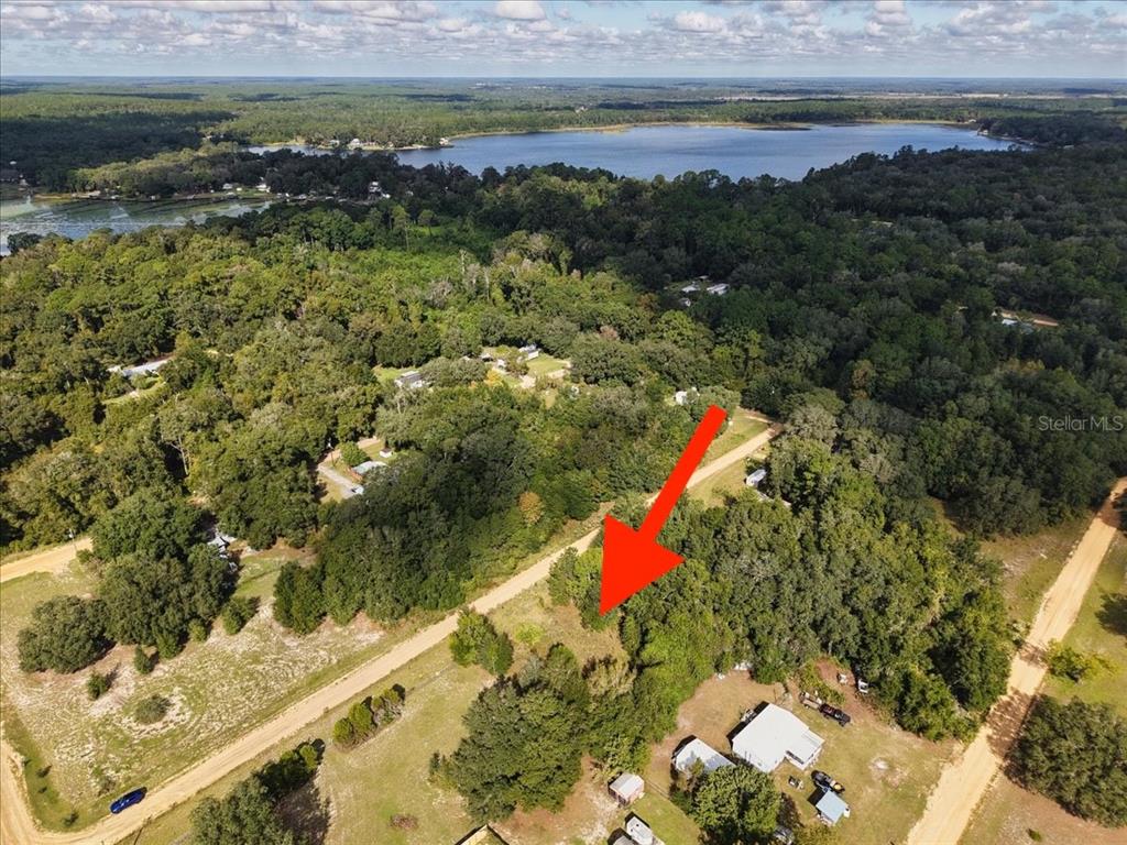 An aerial view shows a wooded lot marked by a red arrow near a lake — 206 N HELMERS AVENUE, INTERLACHEN, FL