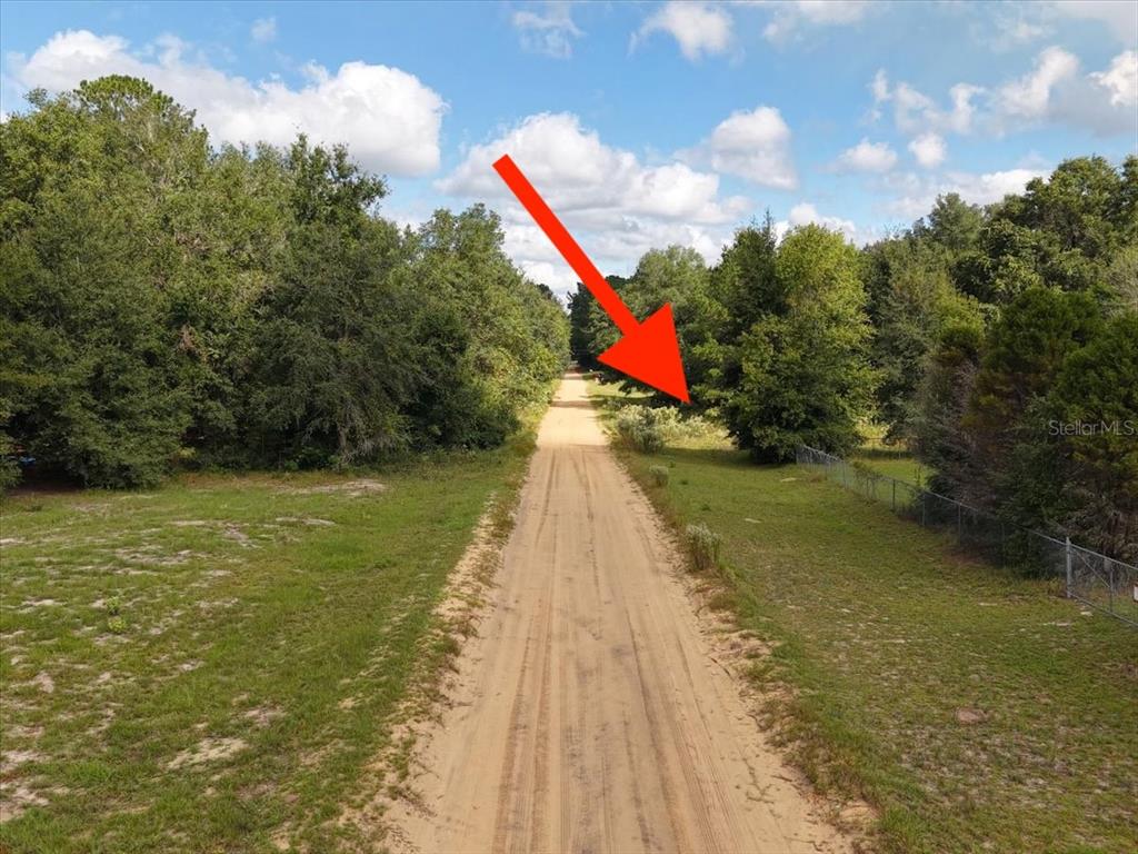 A dirt road runs through a grassy, wooded lot with a chain-link fence on the right — 206 N HELMERS AVENUE, INTERLACHEN, FL
