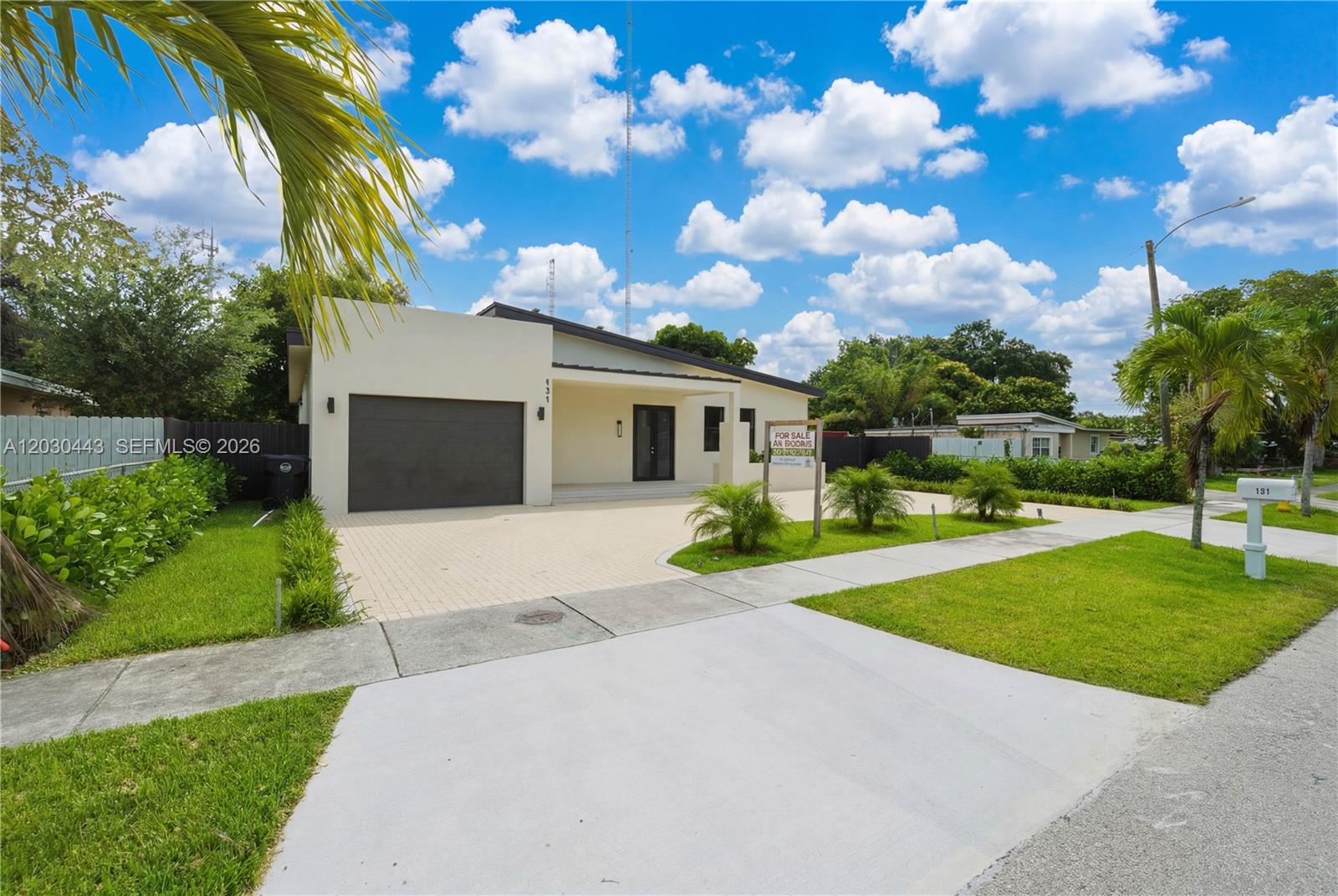 A modern, single-story house with a paved driveway, garage, and palm trees under a blue sky — 131 Miami Gardens Rd, West Park FL 33023, WEST PARK, FL