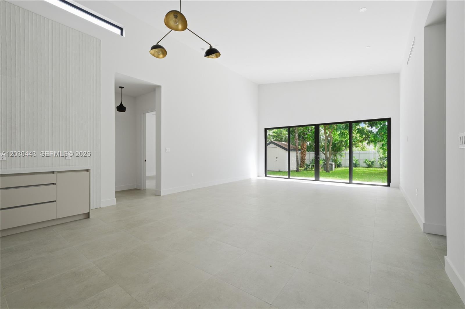 A minimalist living room features white walls, large sliding glass doors, and light tile flooring — 131 Miami Gardens Rd, West Park FL 33023, WEST PARK, FL