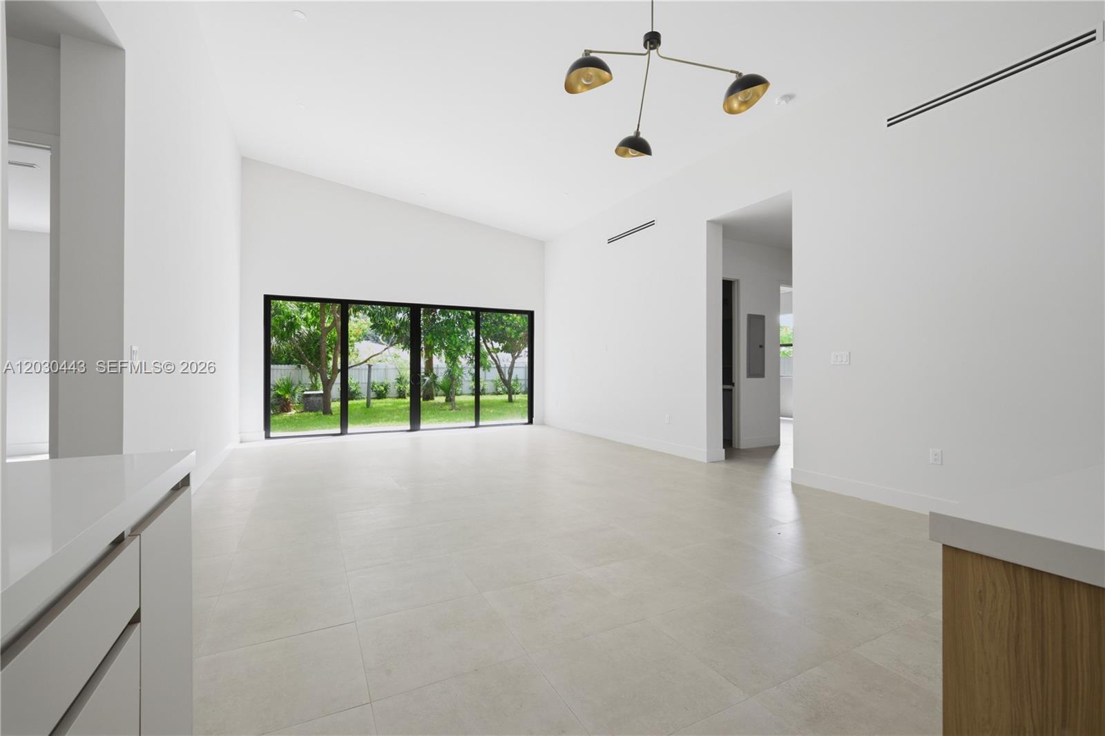 A bright, minimalist living room features white walls, large sliding glass doors, and tile flooring — 131 Miami Gardens Rd, West Park FL 33023, WEST PARK, FL