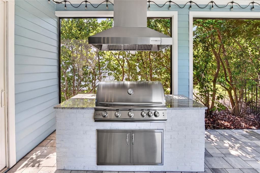 An outdoor kitchen features a stainless steel grill, range hood, and white brick base — 11872 SW 33RD LANE, GAINESVILLE, FL