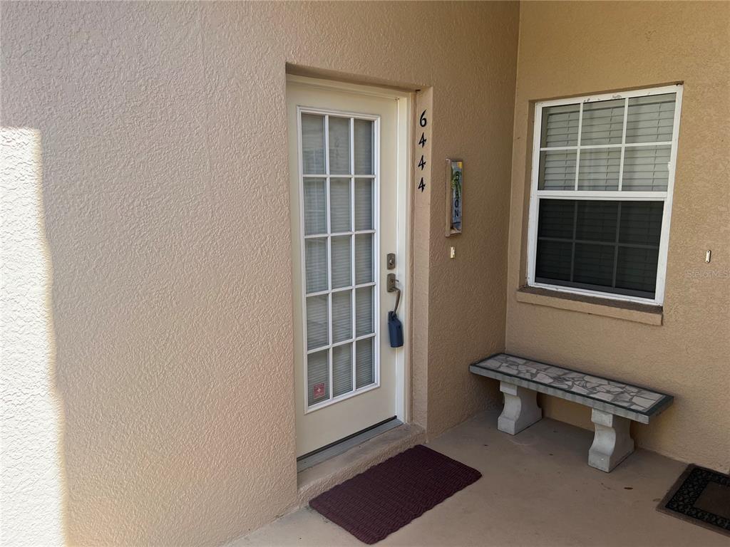 A beige exterior entryway features a glass-paned door, a window, and a stone bench — 6444 7TH AVENUE CIRCLE W UNIT 6444, BRADENTON, FL