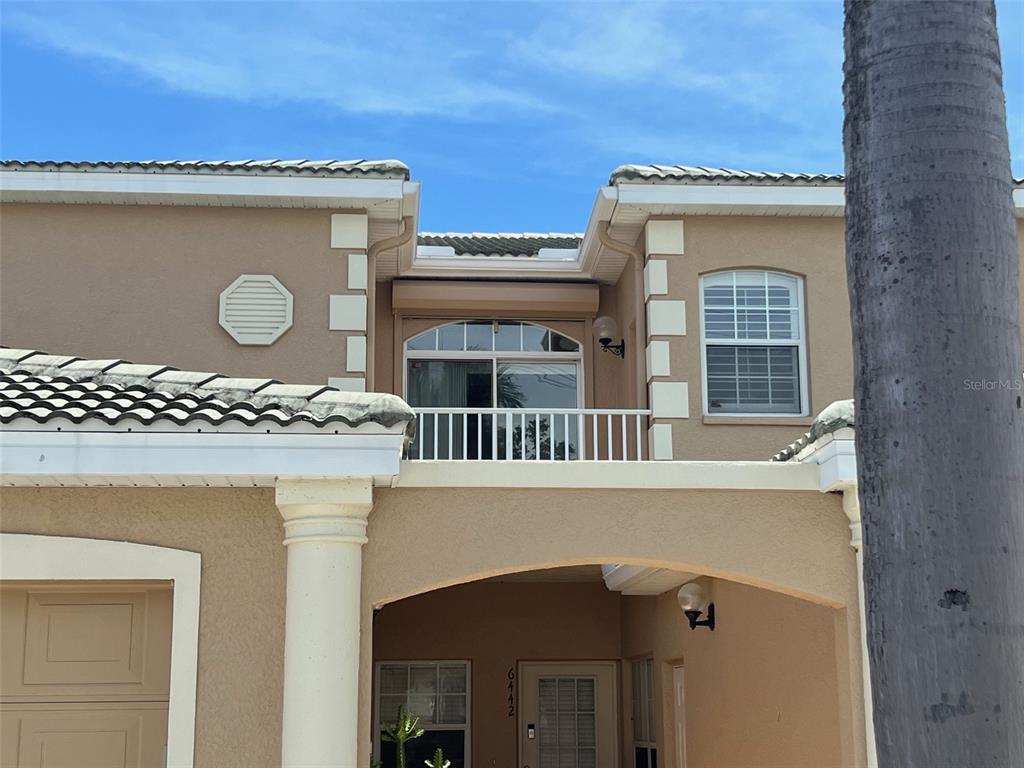 The exterior of a two-story stucco home features a second-floor balcony and arched entryway — 6444 7TH AVENUE CIRCLE W UNIT 6444, BRADENTON, FL