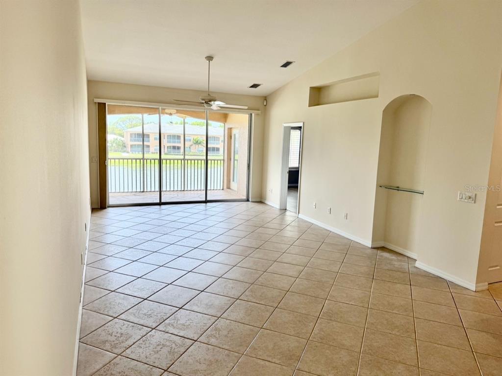 An empty living room with beige tile floors, a ceiling fan, and sliding glass balcony doors — 6444 7TH AVENUE CIRCLE W UNIT 6444, BRADENTON, FL