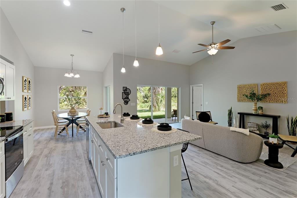 An open-concept kitchen and living area features a granite island, light wood flooring, and vaulted ceilings — 3840 ADELAIDE AVENUE, NORTH PORT, FL
