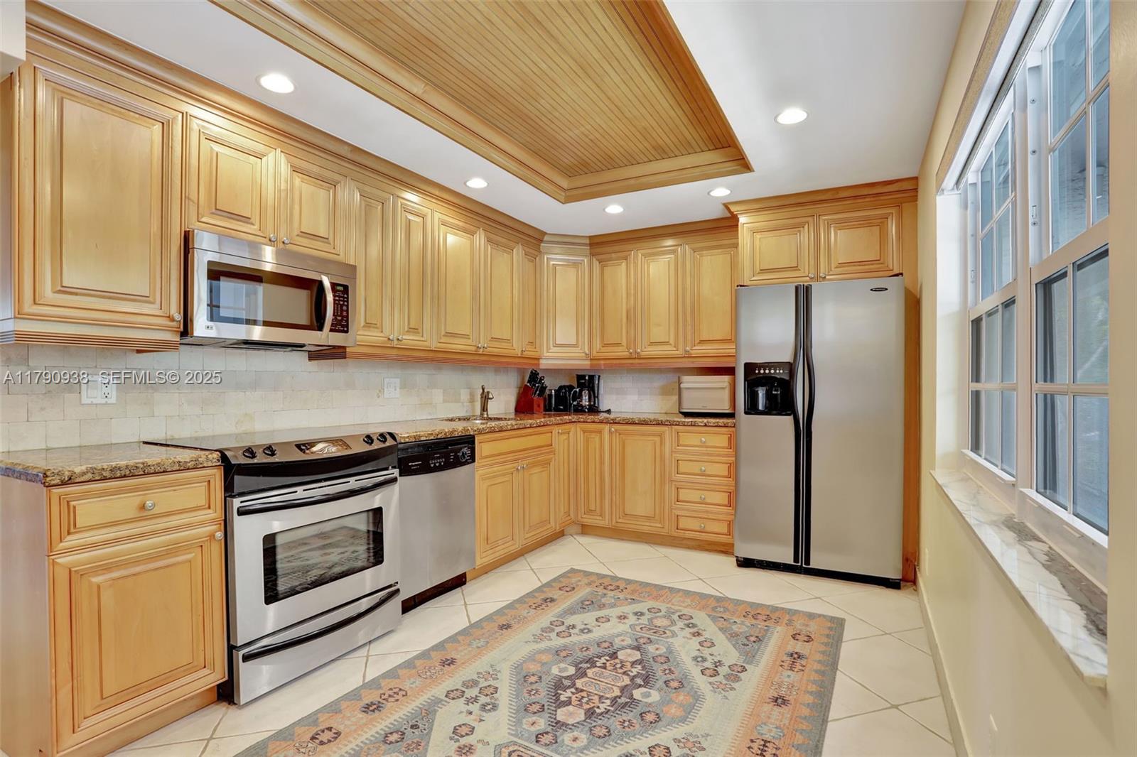 A kitchen with light wood cabinets, stainless steel appliances, tile flooring, and a patterned rug — 4020 W Palm Aire Dr # 204, Pompano Beach FL 33069, POMPANO BEACH, FL