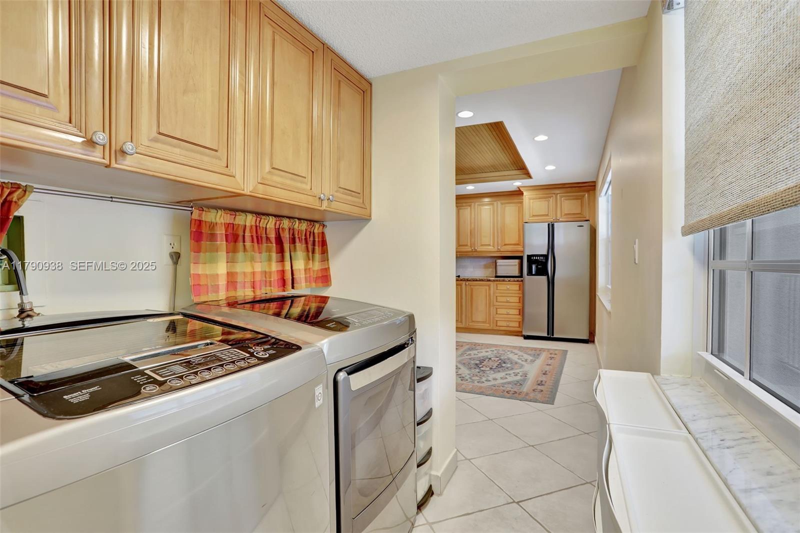 A laundry room with stainless steel appliances leads into a kitchen with light wood cabinets — 4020 W Palm Aire Dr # 204, Pompano Beach FL 33069, POMPANO BEACH, FL