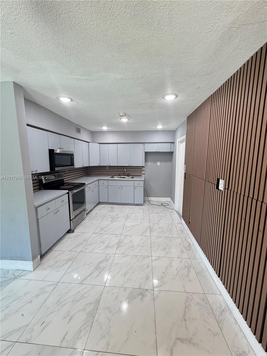 A kitchen features light gray cabinets, stainless steel appliances, marble-look tile floors, and wood-slat walls — 850 NW 113th St, Miami FL 33168, MIAMI, FL