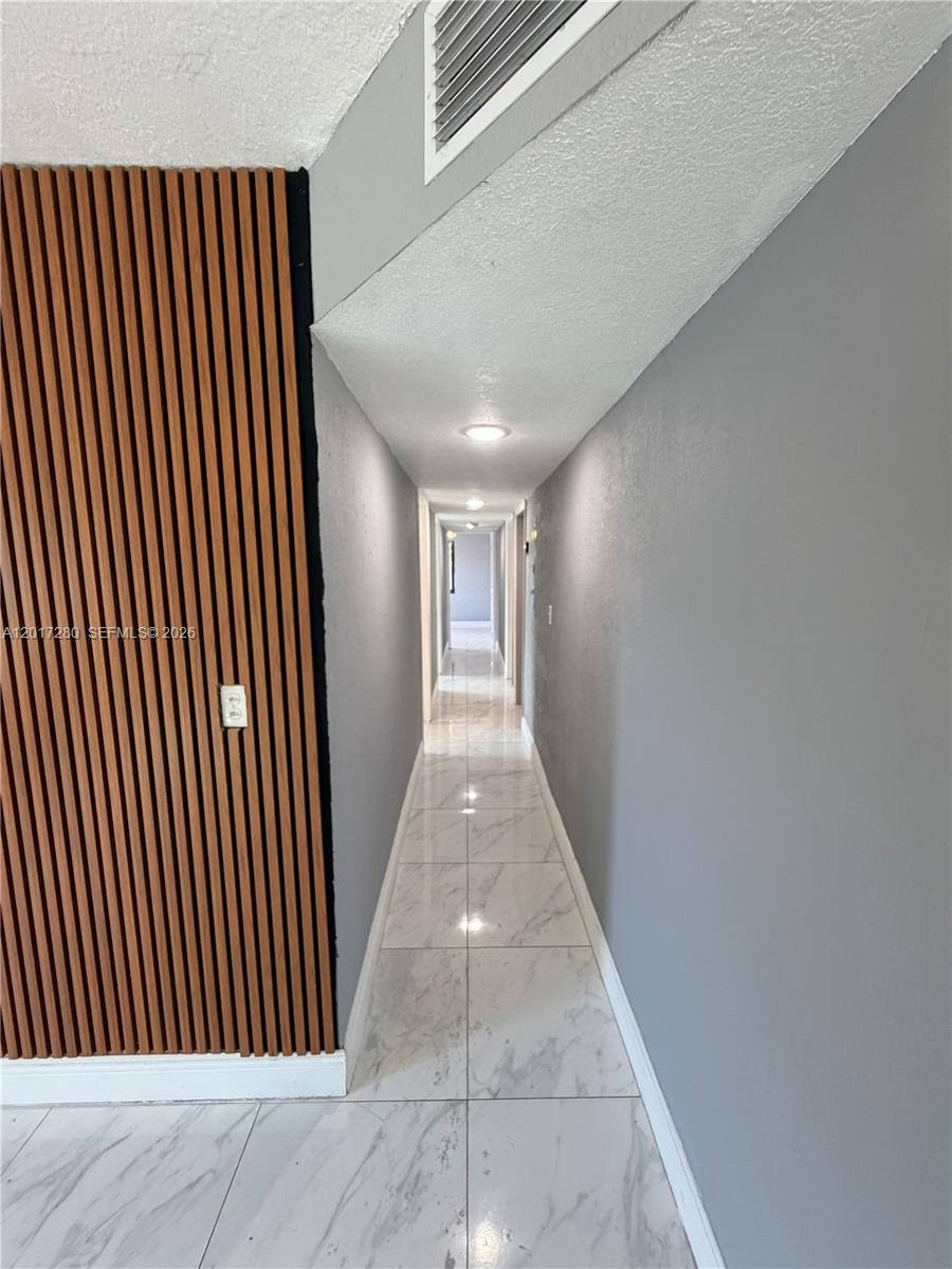 A long hallway features gray walls, white marble-style tile flooring, and a wood-slatted accent wall — 850 NW 113th St, Miami FL 33168, MIAMI, FL