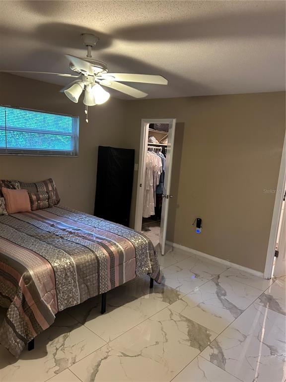 A bedroom features a bed with patterned bedding, a ceiling fan, and white marble-look tile flooring — 1016 KIRK STREET, ORLANDO, FL