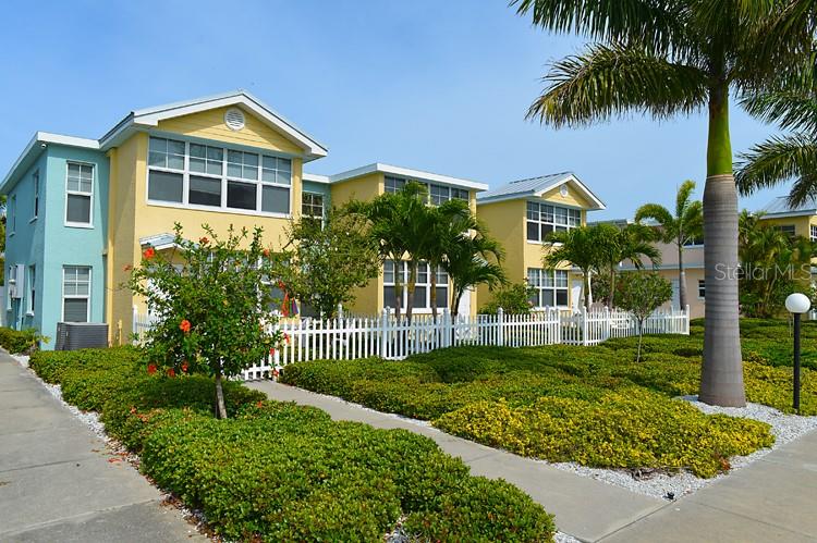 A multi-story yellow and blue building with a white fence and palm trees — 19417 GULF BOULEVARD UNIT A202, INDIAN SHORES, FL