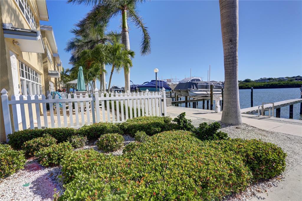 A white picket fence borders a landscaped garden next to a waterfront boat dock — 19417 GULF BOULEVARD UNIT A202, INDIAN SHORES, FL