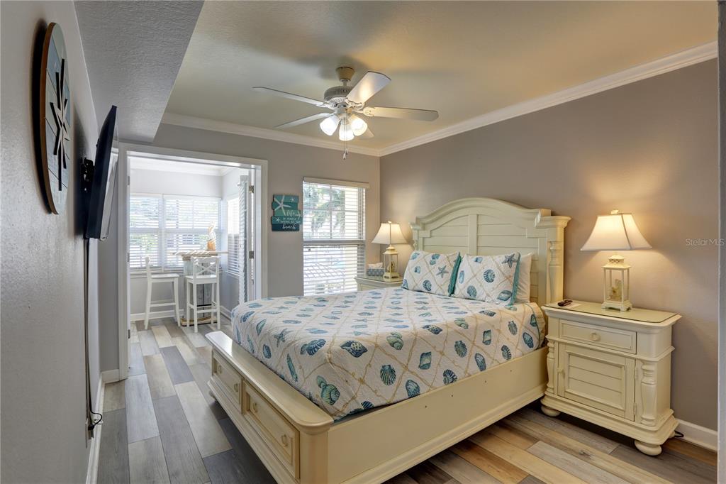 A bedroom features a queen bed with seashell bedding, a ceiling fan, and an attached sunroom — 19417 GULF BOULEVARD UNIT A202, INDIAN SHORES, FL