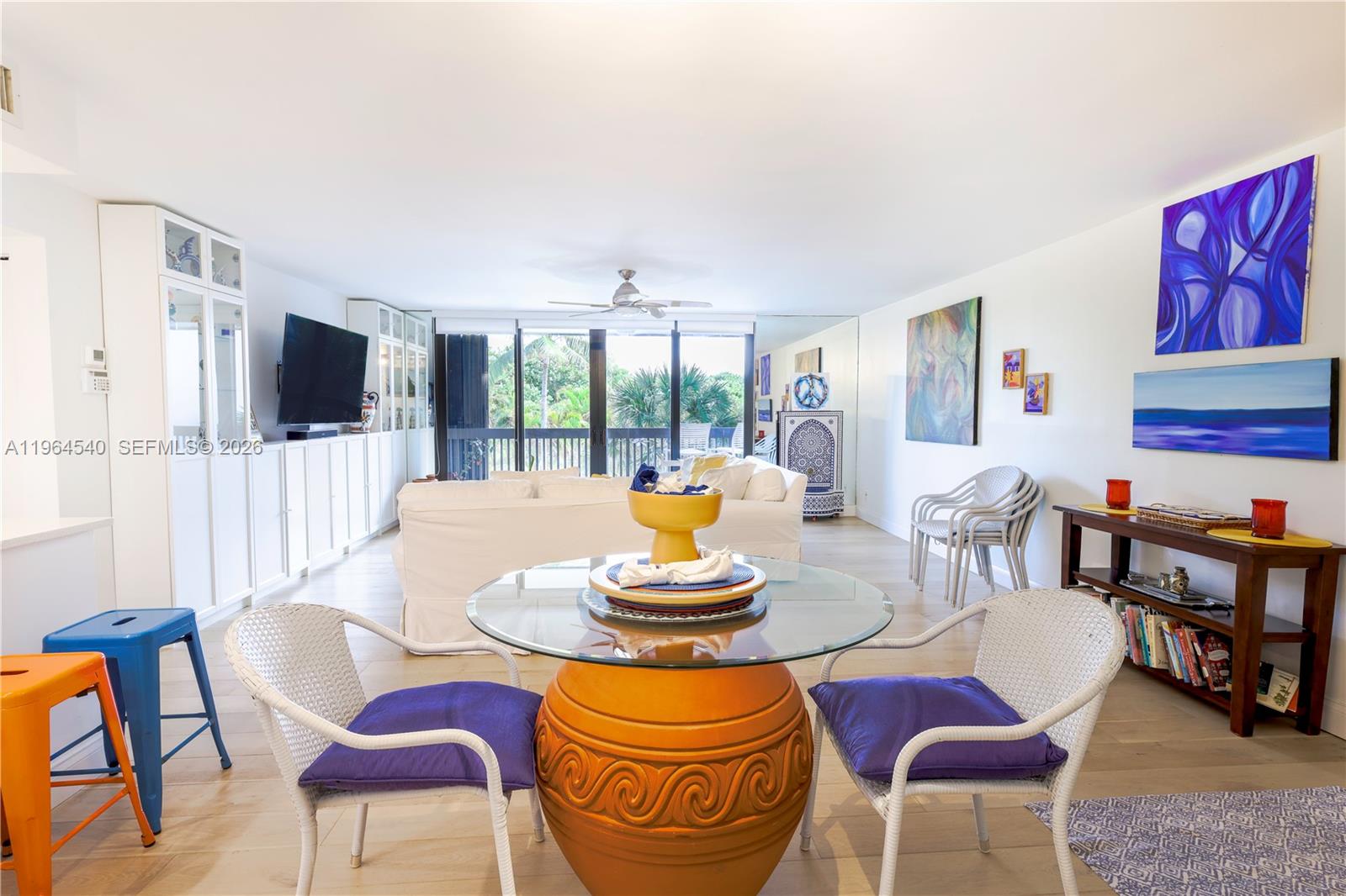 A living and dining area features a glass-topped table, white furniture, and colorful wall art — 4201 N Ocean Dr # 304, Hollywood FL 33019, HOLLYWOOD, FL